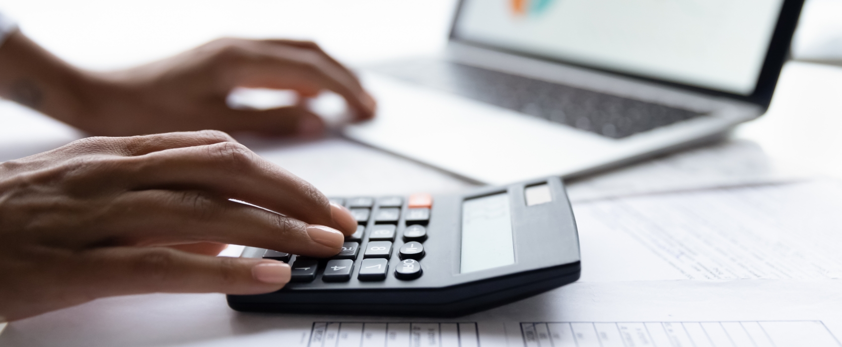 An Introductory Guide to Dental Practice Financing Hands using a calculator beside a laptop and financial documents, representing budgeting and planning for dental practice financing.