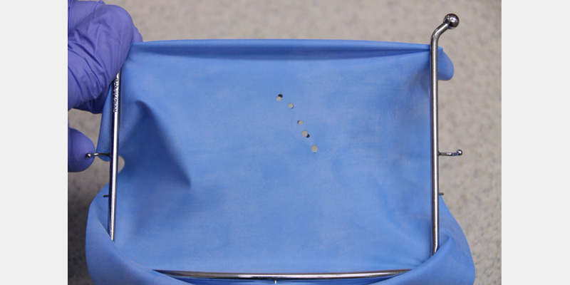 efrver Rubber dam mounted on a frame with punched holes spaced to match the dental arch for multiple-tooth isolation.
