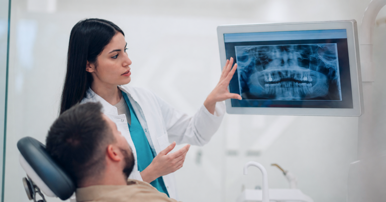 Spear Digest Dentist reviewing digital X-rays with a patient as part of structured doctor development in DSOs focused on clinical communication and treatment planning.