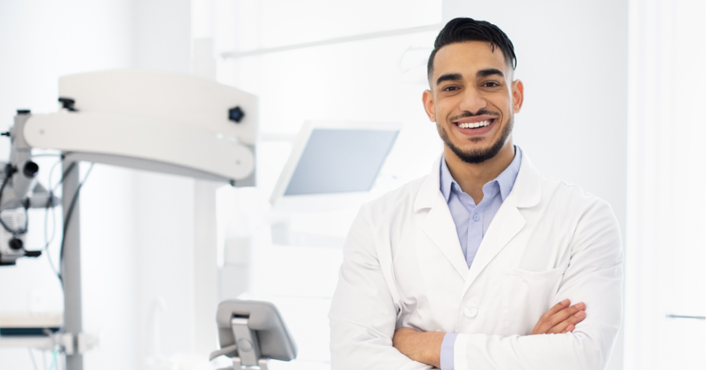 Essential New Dentist Career Advice for Your First 5 Years New dentist career advice hero image of a smiling early-career dentist standing with arms crossed in a dental operatory