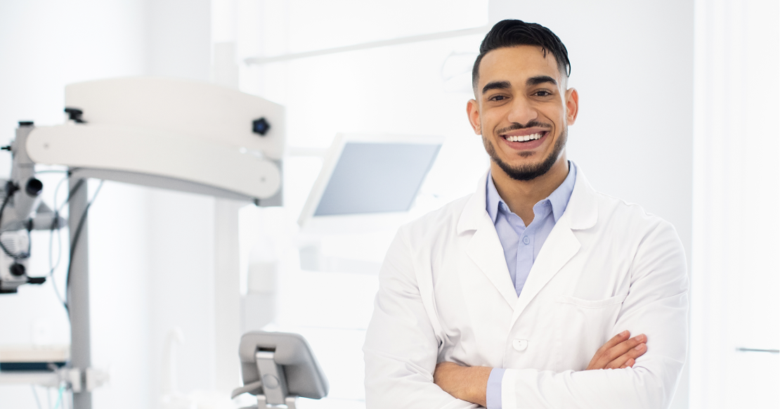New dentist career advice hero image of a smiling early-career dentist standing with arms crossed in a dental operatory